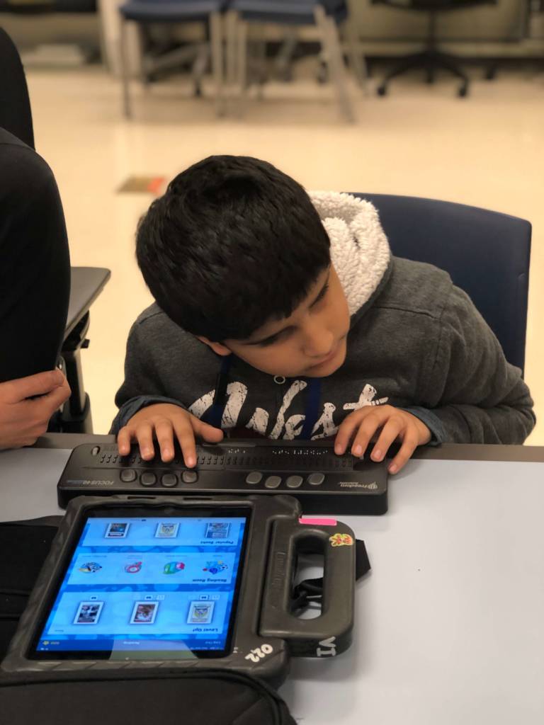 A boy uses a refreshable braille display paired with an iPad.