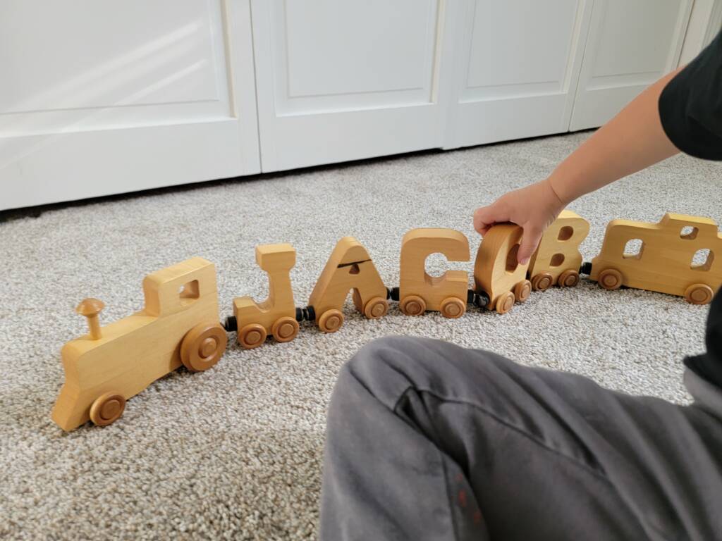 A student playing with a wooden train with individual letters spelling JACOB.