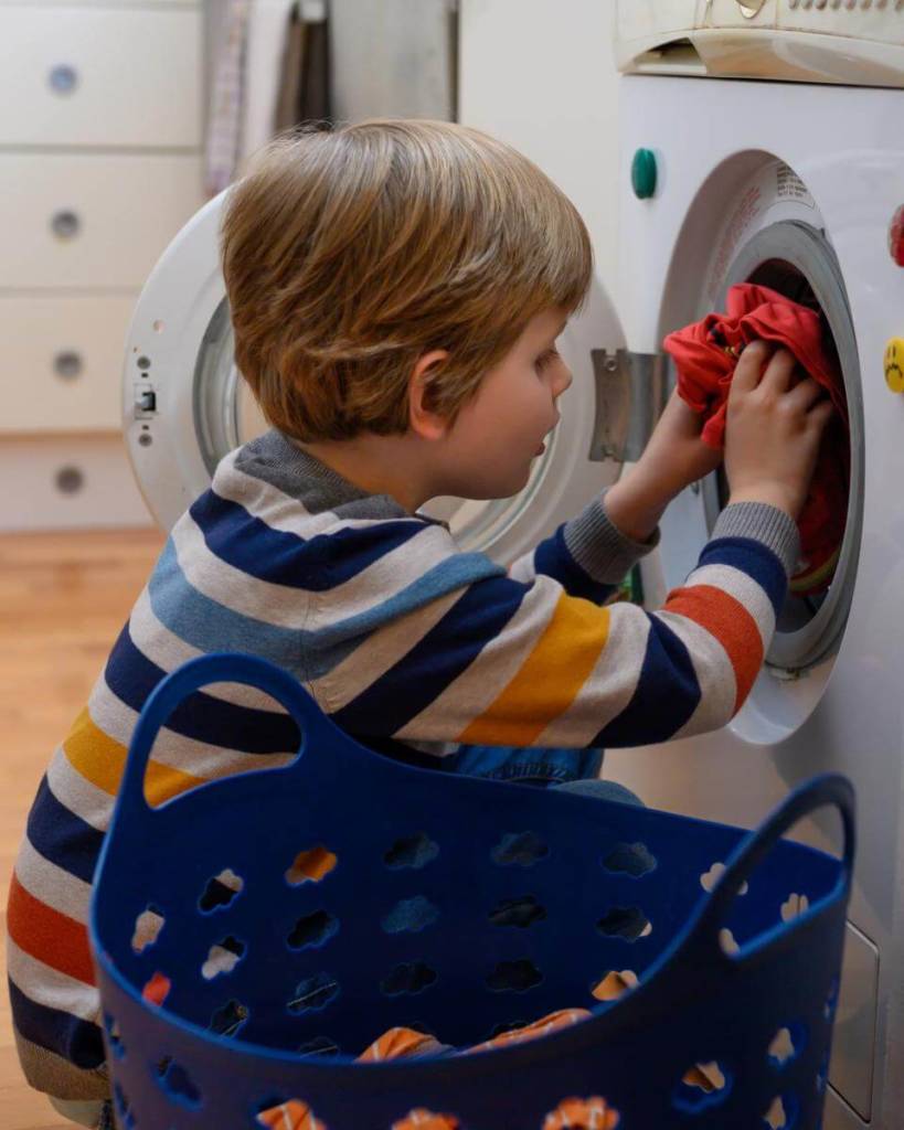 A young boy places clothes in the washing machine