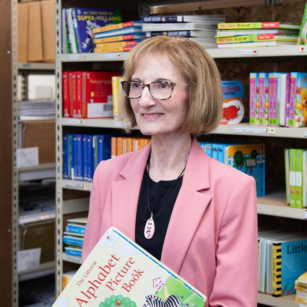 Debra Bonde holding an alphabet book in front of a shelf of books.