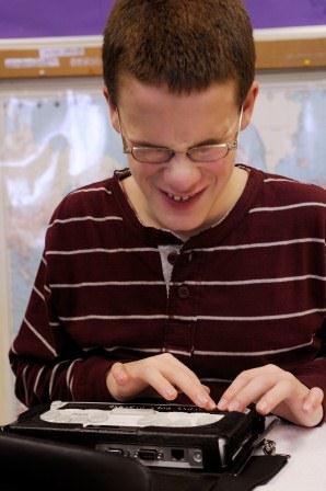 A boy wearing glasses uses a braillenote