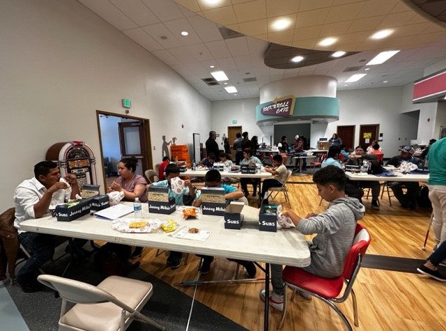 A cafeteria with parents and children eating lunch together.