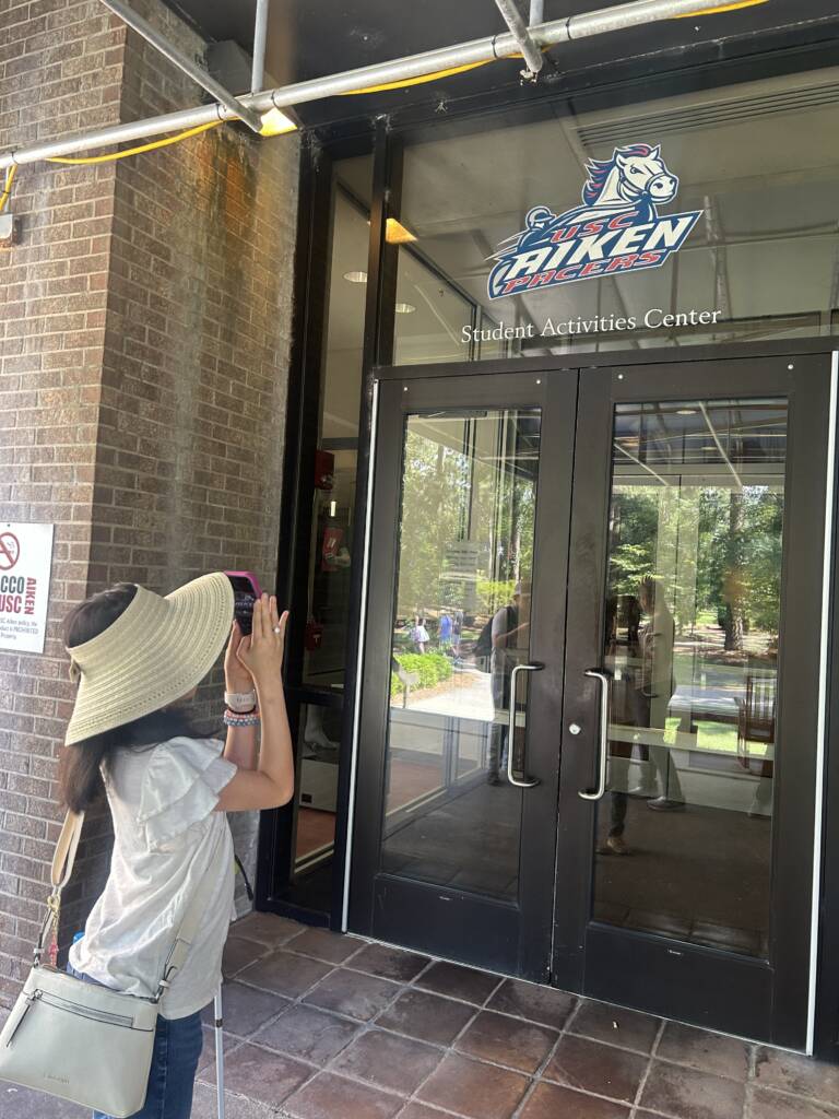 A female traveler uses zoom on her iPhone to verify the sign above a building’s door. 