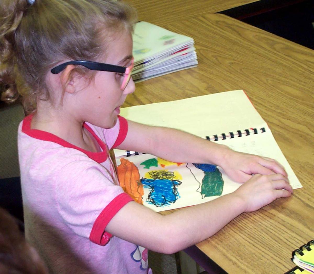 Haylee enjoys reading a book she authored and illustrated. Haylee reading a book that has pictures she has colored.