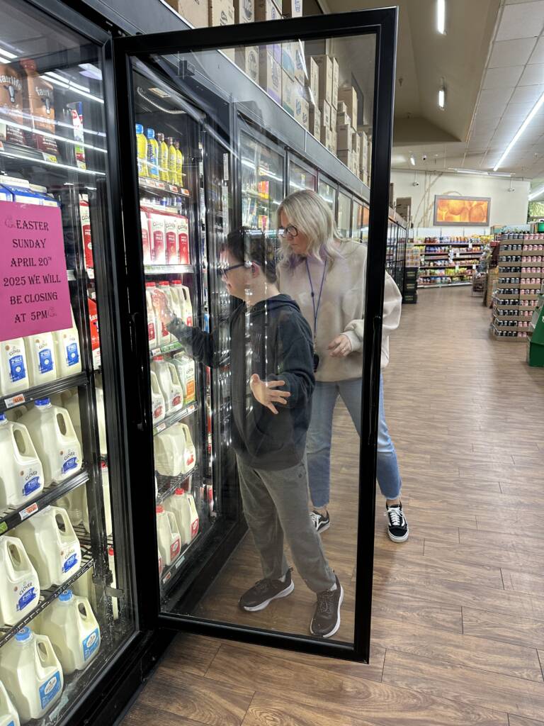 Student with teacher behind them, is opening the glass door to get a 1/2 gallon of milk.