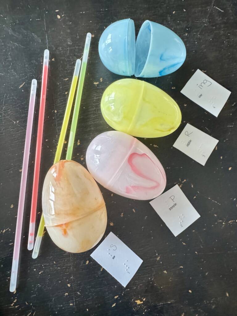Four plastic Easter egg with light up glow stick and four little cards that have braille S, P, R, ING.