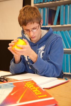 Boy with glasses tactually examines a manipulative illustrating geometrical shapes.
