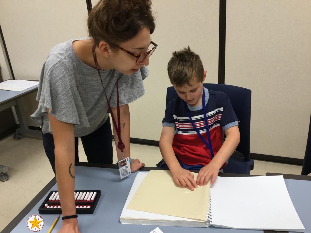 Student examining tactile graphics while teacher looks on