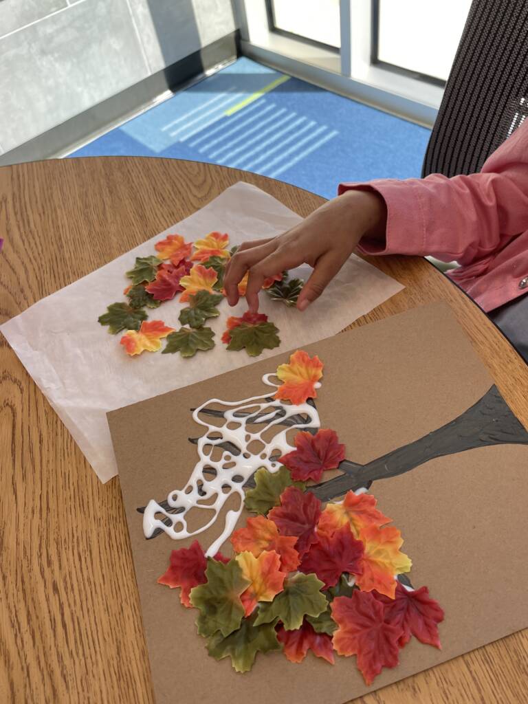 Student putting plastic leaves onto a the top of the tree with lots of elmer's glue on it. 