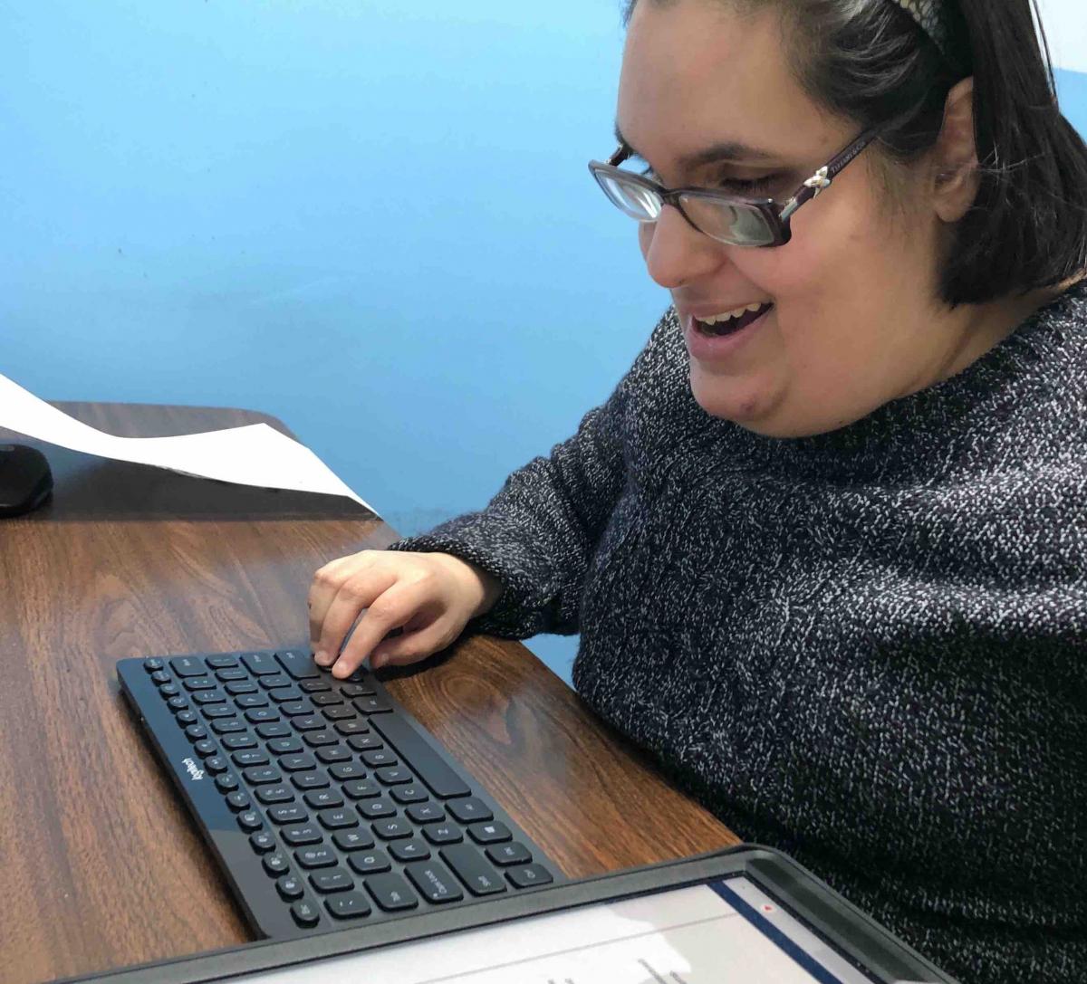 Student smiling as she types her story about the Indian food that she likes to eat. She is typing in the Voice Dream Writer app via a Bluetooth keyboard connected to an iPad. Student typing story about Indian Food