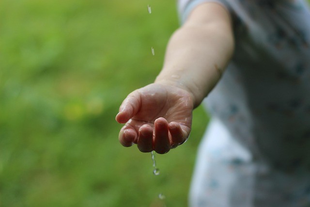 Child's hand held out to feel a rain drop outside.