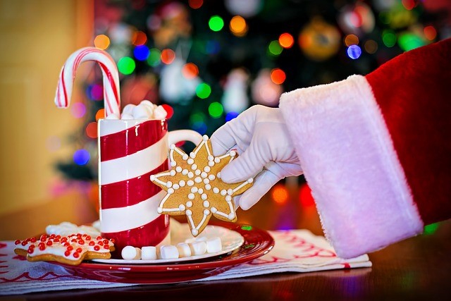 Santa getting a cookie off a plate with treats and hot cocoa.