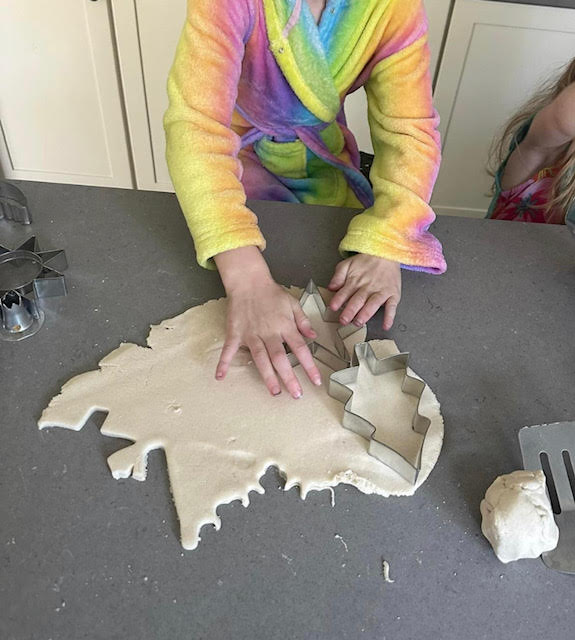 Child using a cookie cutter shaped like a tree to cut out a tree shape from the salt dough.