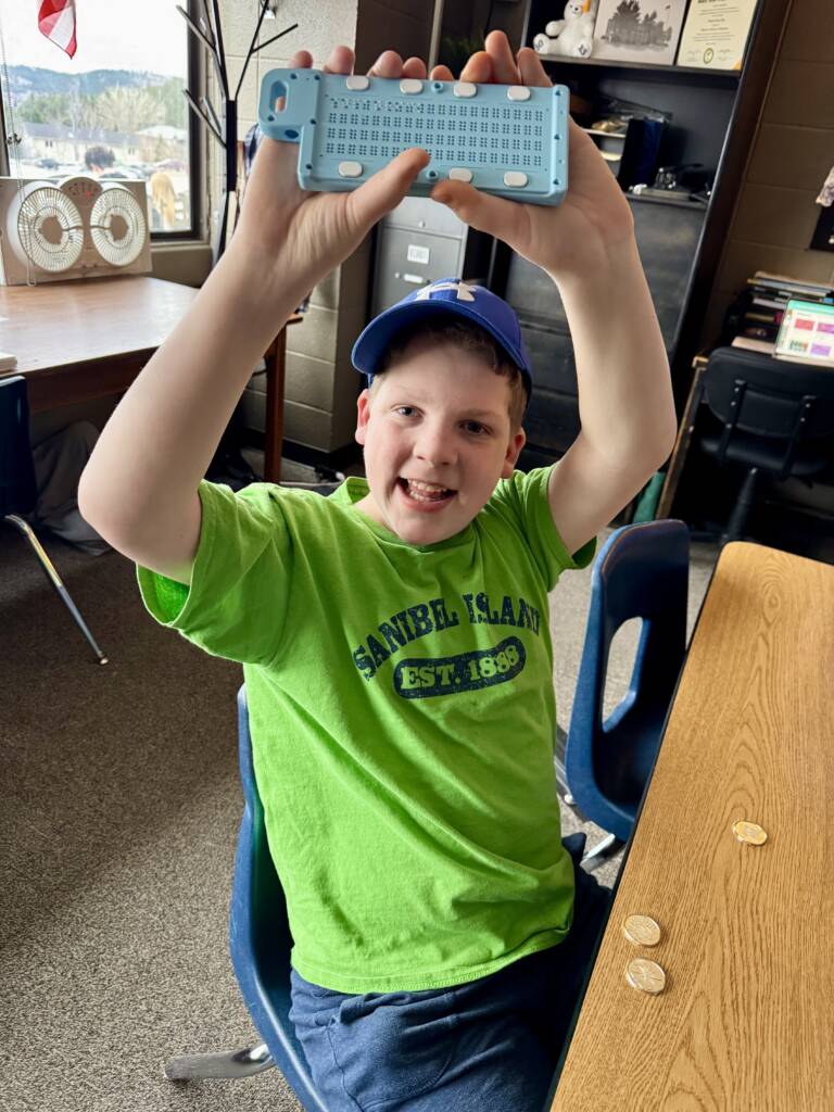 Liam happily holding up the Versa slate with gold coins on the table in front of him. 