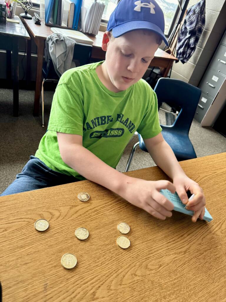 Liam using the Versa slate on a table with gold coins next to him. 