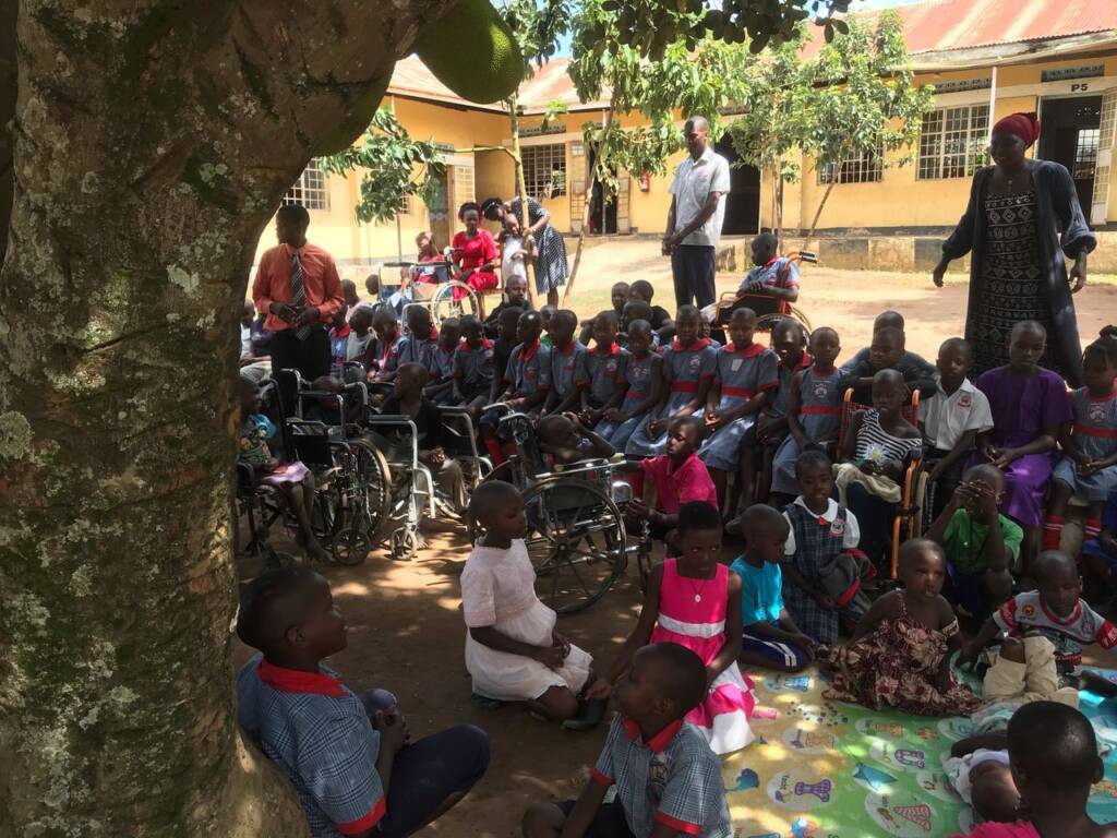 A large group of students with their teachers sitting under a tree outside of their school in Uganda.