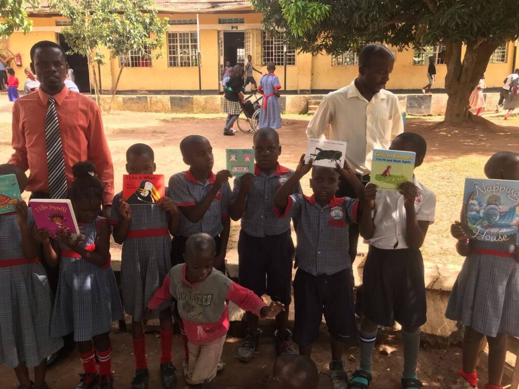 Students in a line outside of their school in Uganda with their teachers holding up the braille and print books. 