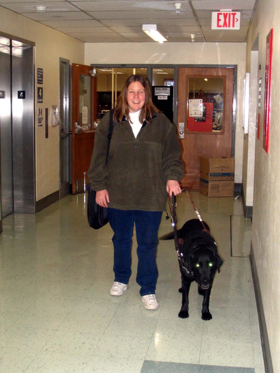 Anna and her dog guide walk down a hallway in a college building.