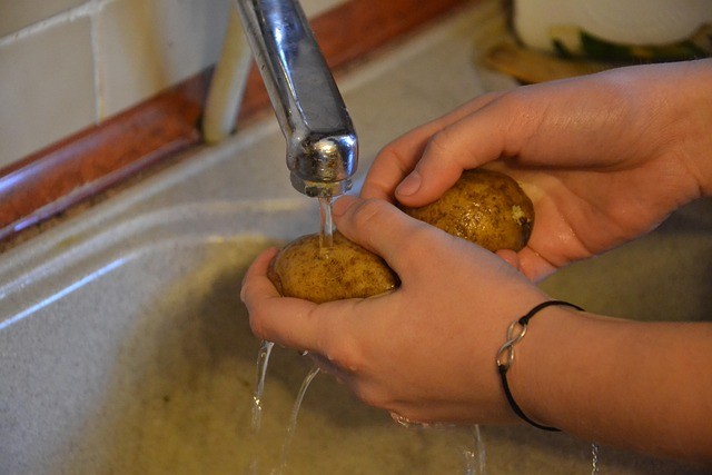 hands washing potatoes at the kitchen sink.