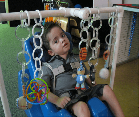 A young boy in an adapted seat gazes at a mobile.