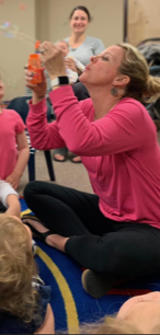 Teacher blowing bubbles with her young students around her.